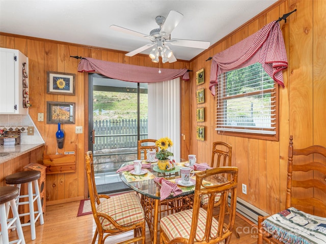 dining room with ceiling fan, wooden walls, baseboard heating, light wood-type flooring, and crown molding