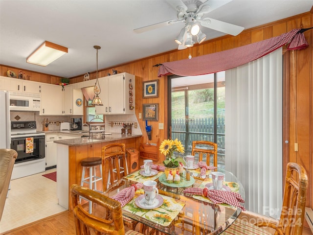 dining room with light wood-type flooring, wood walls, a baseboard heating unit, and ceiling fan