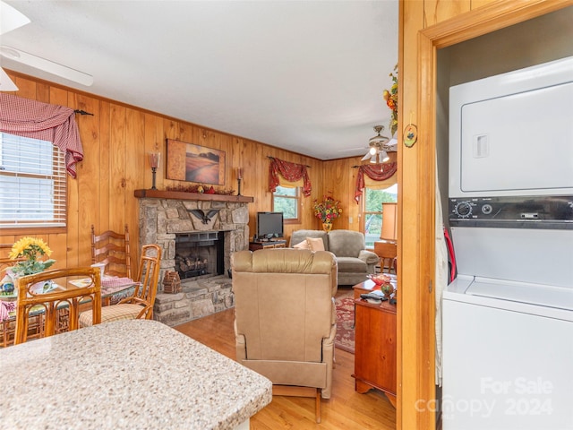 living room with a stone fireplace, wooden walls, light hardwood / wood-style flooring, and stacked washer / dryer