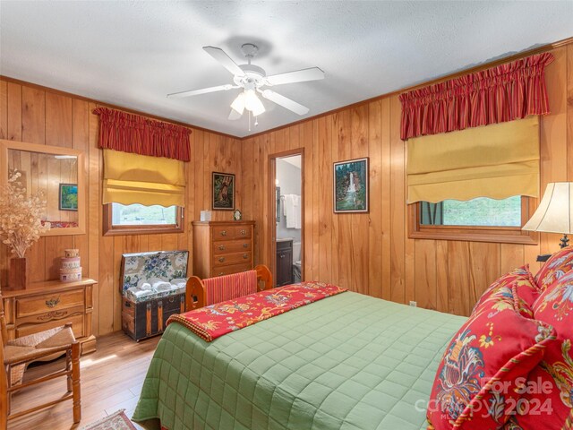 bedroom with wooden walls, ensuite bath, light hardwood / wood-style floors, and ceiling fan