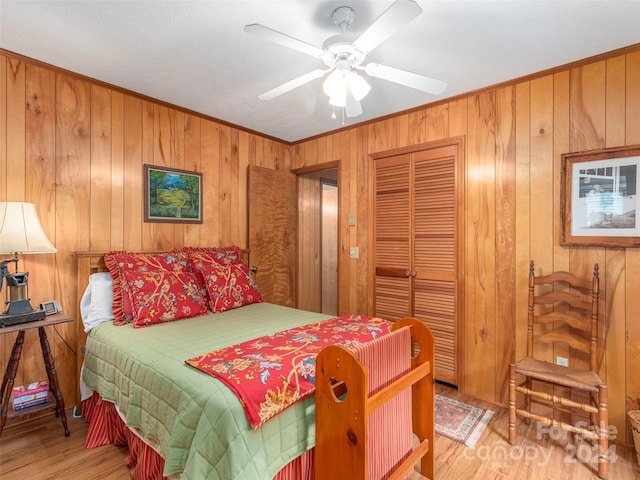 bedroom featuring ceiling fan, wooden walls, light hardwood / wood-style flooring, and a closet