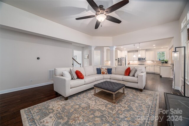 living room featuring ceiling fan, decorative columns, and dark hardwood / wood-style floors