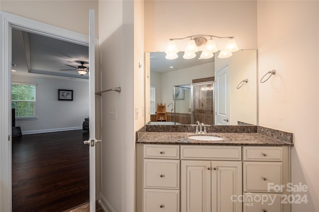 full bath featuring baseboards, wood finished floors, vanity, a raised ceiling, and a ceiling fan