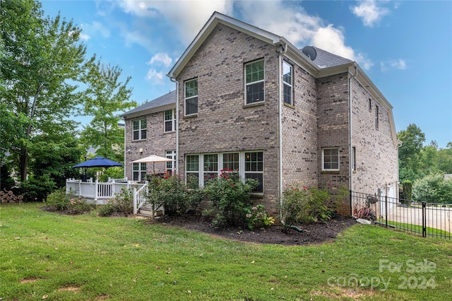 back of property featuring a lawn, a deck, brick siding, and fence
