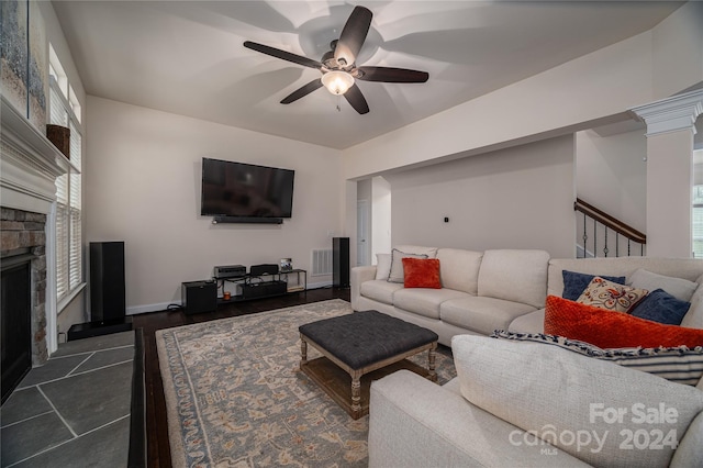 living room featuring ornate columns, ceiling fan, dark hardwood / wood-style floors, and a stone fireplace