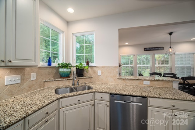 kitchen with light stone counters, a sink, decorative backsplash, hanging light fixtures, and stainless steel dishwasher