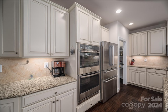 kitchen with light stone counters, dark wood-style floors, appliances with stainless steel finishes, white cabinets, and decorative backsplash