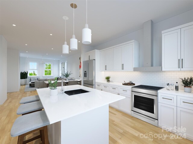 kitchen featuring a kitchen island with sink, stainless steel appliances, sink, white cabinets, and wall chimney range hood