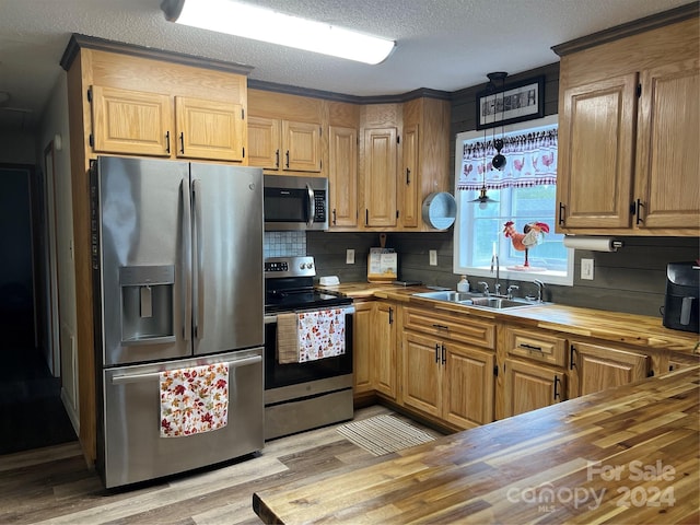 kitchen featuring a sink, a textured ceiling, stainless steel appliances, butcher block counters, and light wood finished floors