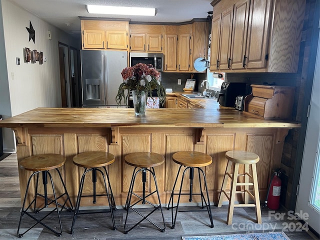 kitchen with a sink, stainless steel appliances, a peninsula, and wood counters