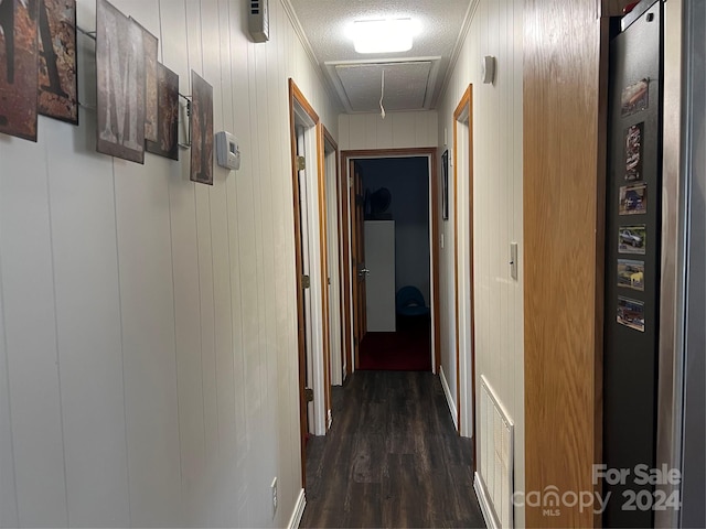 corridor featuring visible vents, dark wood-type flooring, attic access, ornamental molding, and a textured ceiling