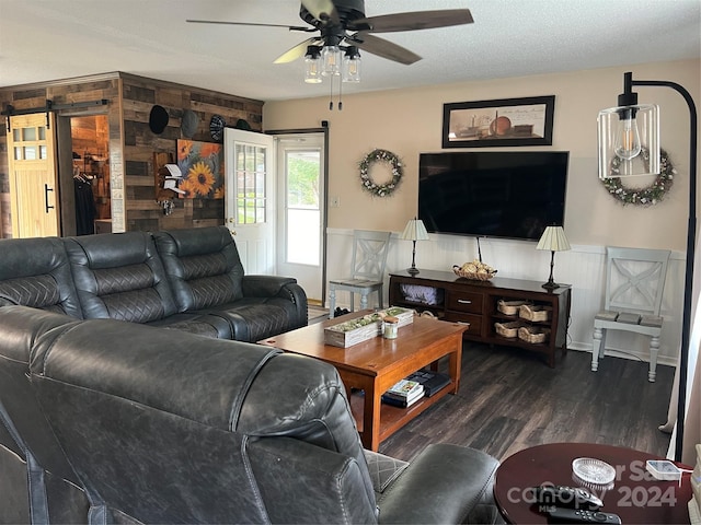 living area featuring ceiling fan, a textured ceiling, dark wood-type flooring, and a barn door