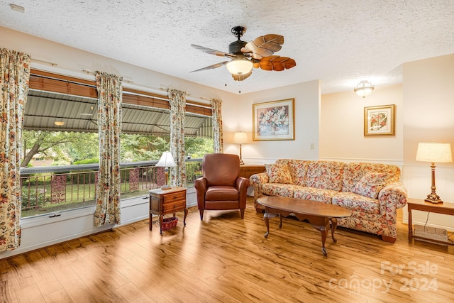 living room with light hardwood / wood-style floors, ceiling fan, and a textured ceiling