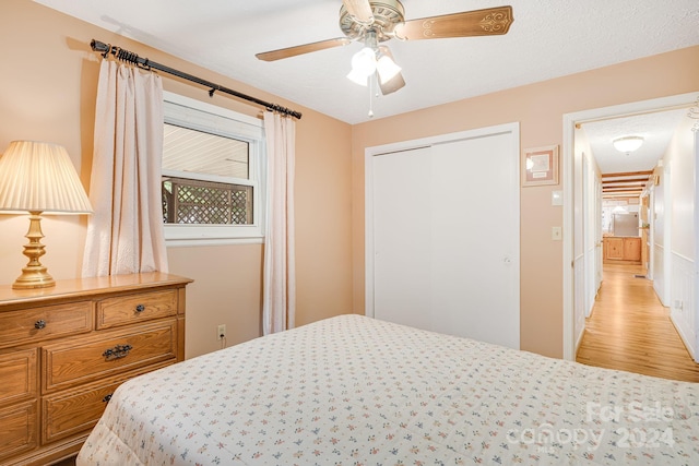 bedroom with a closet, light wood-type flooring, ceiling fan, and a textured ceiling