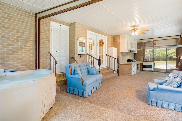 living room with brick wall, light colored carpet, and ceiling fan