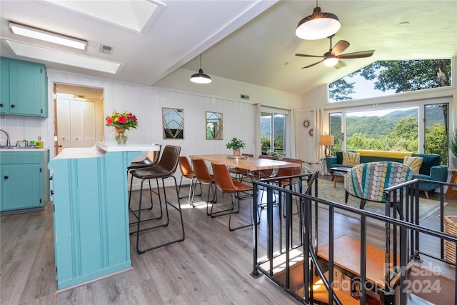 dining area featuring light hardwood / wood-style flooring, vaulted ceiling with skylight, sink, and ceiling fan