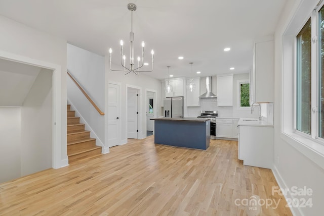 kitchen with stainless steel appliances, wall chimney range hood, pendant lighting, white cabinets, and a kitchen island