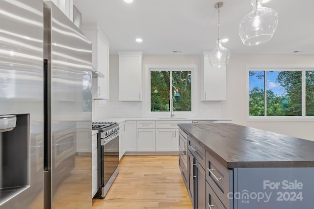 kitchen featuring wood counters, light wood-type flooring, decorative light fixtures, white cabinetry, and stainless steel appliances