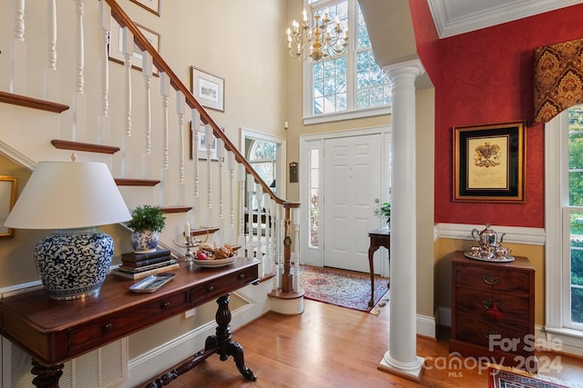 entrance foyer featuring a towering ceiling, wood-type flooring, ornamental molding, and ornate columns