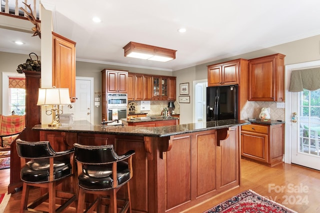 kitchen featuring light wood-type flooring, black fridge with ice dispenser, kitchen peninsula, and a breakfast bar