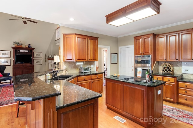 kitchen featuring dark stone countertops, stainless steel double oven, kitchen peninsula, ceiling fan, and light hardwood / wood-style floors