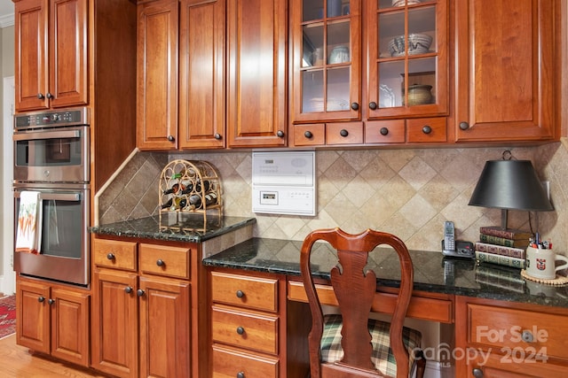 kitchen featuring built in desk, dark stone counters, double oven, and tasteful backsplash