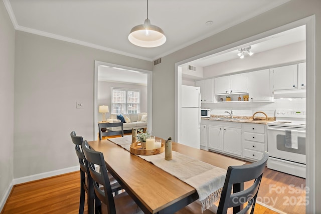 dining room with sink, light hardwood / wood-style flooring, and ornamental molding