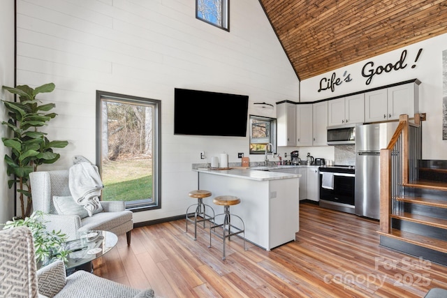 kitchen featuring a kitchen bar, high vaulted ceiling, kitchen peninsula, stainless steel appliances, and white cabinets