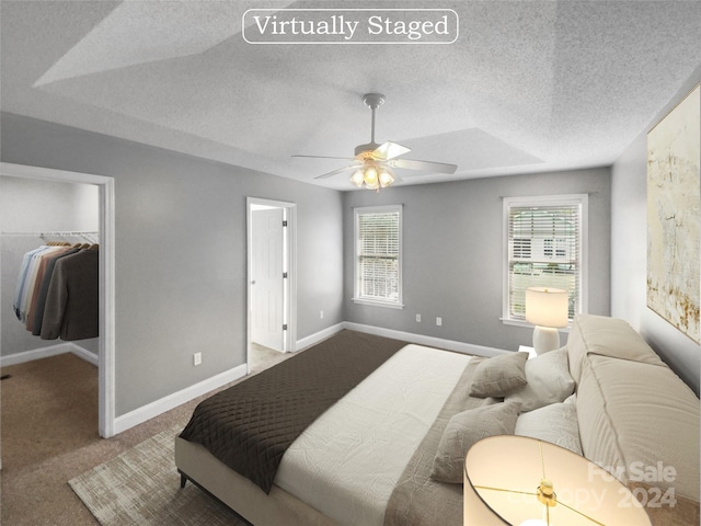 carpeted bedroom featuring a textured ceiling, ceiling fan, a closet, a tray ceiling, and a spacious closet