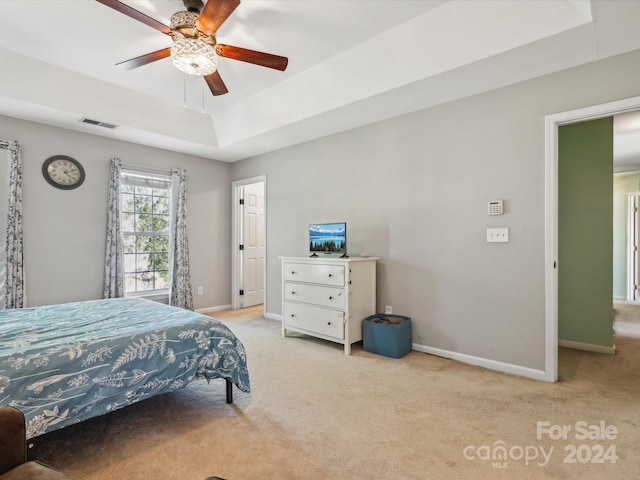 bedroom with light colored carpet, a tray ceiling, and ceiling fan