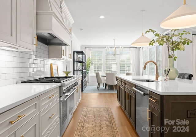 kitchen featuring an island with sink, sink, tasteful backsplash, stainless steel appliances, and light wood-type flooring