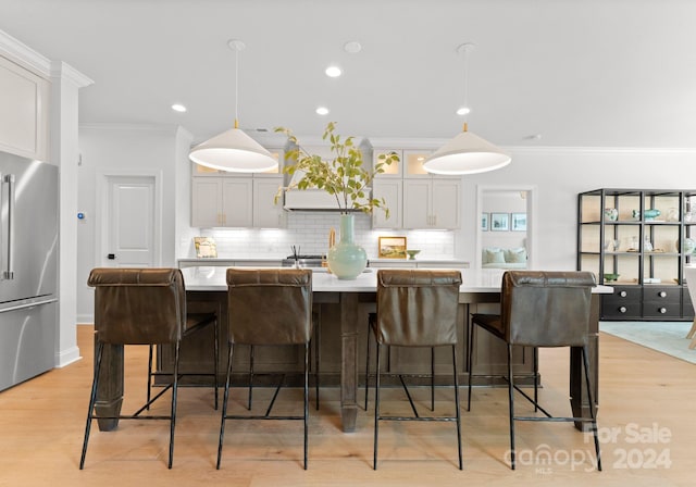 kitchen featuring light hardwood / wood-style flooring, decorative light fixtures, white cabinetry, stainless steel refrigerator, and a kitchen bar