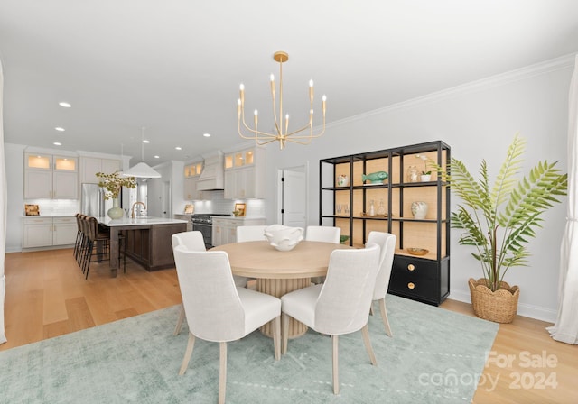 dining space with ornamental molding, light wood-type flooring, an inviting chandelier, and sink