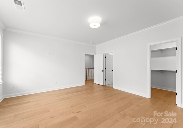 unfurnished bedroom with light wood-type flooring, crown molding, a walk in closet, and a closet