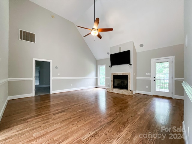 unfurnished living room with high vaulted ceiling, ceiling fan, a tile fireplace, and light wood-type flooring