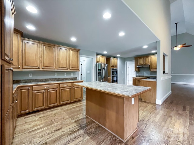 kitchen featuring black double oven, light wood-type flooring, stainless steel refrigerator with ice dispenser, ceiling fan, and a kitchen island