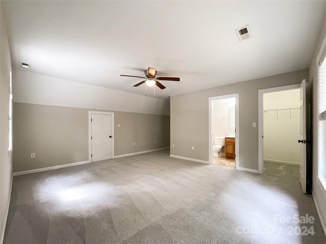 unfurnished bedroom featuring light carpet, a walk in closet, a closet, ceiling fan, and connected bathroom