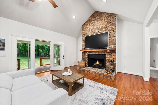living area featuring high vaulted ceiling, baseboards, ceiling fan, wood finished floors, and a stone fireplace
