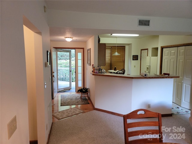 interior space featuring carpet flooring, white fridge with ice dispenser, and kitchen peninsula