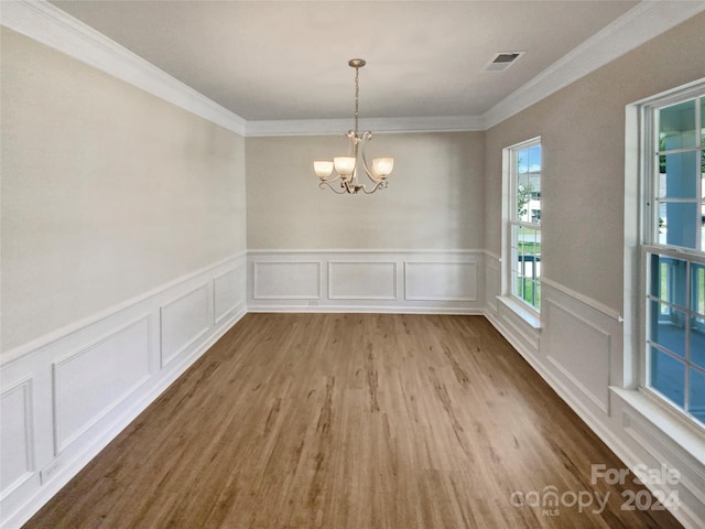 unfurnished dining area featuring light wood-type flooring, crown molding, and an inviting chandelier