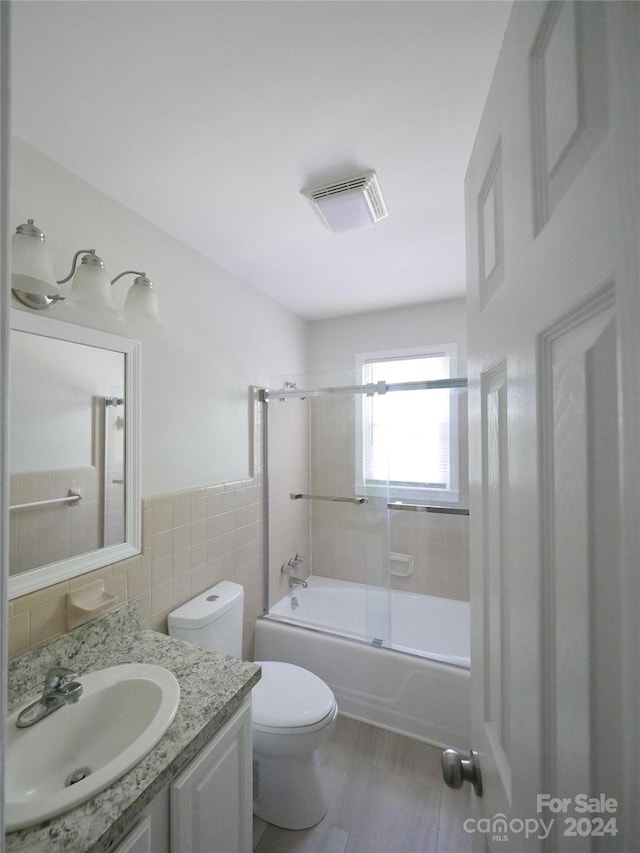 full bathroom with tile walls, combined bath / shower with glass door, vanity, and toilet