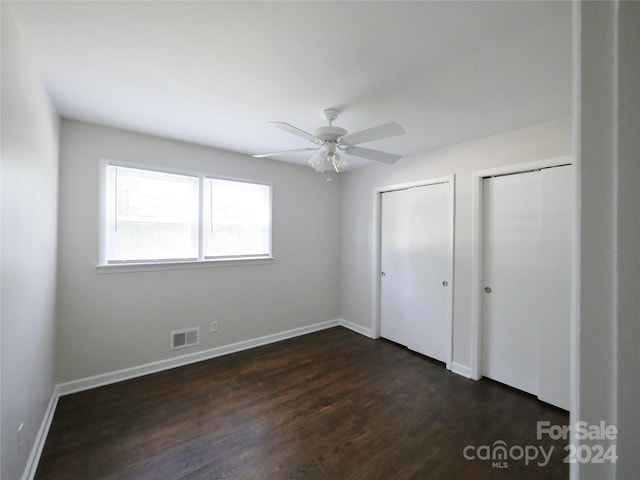 unfurnished bedroom with ceiling fan, multiple closets, and dark hardwood / wood-style floors