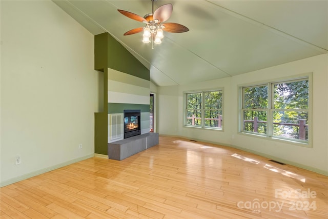 unfurnished living room with high vaulted ceiling, ceiling fan, a tiled fireplace, and light wood-type flooring