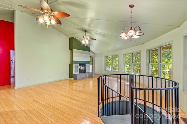 interior space featuring a ceiling fan, wood finished floors, lofted ceiling, a multi sided fireplace, and baseboards