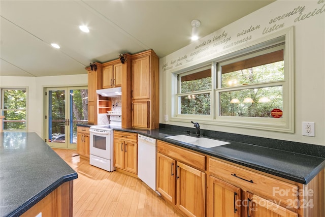 kitchen with a sink, under cabinet range hood, white appliances, dark countertops, and light wood-style floors