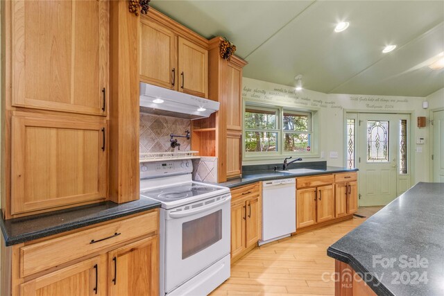 kitchen featuring a sink, lofted ceiling, under cabinet range hood, white appliances, and dark countertops