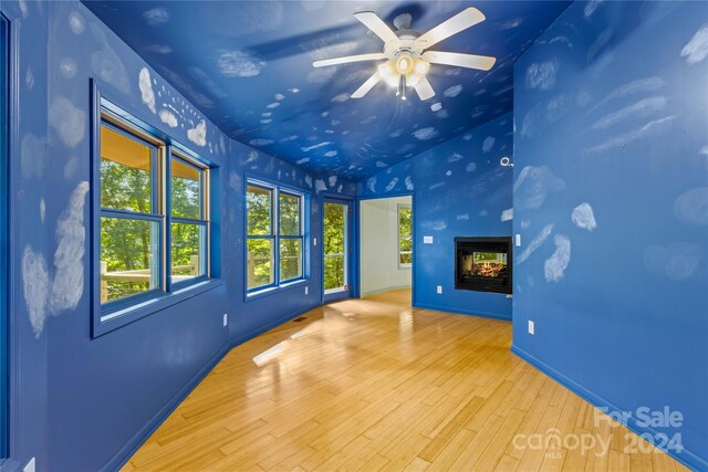unfurnished living room with wood finished floors, vaulted ceiling, baseboards, ceiling fan, and a multi sided fireplace