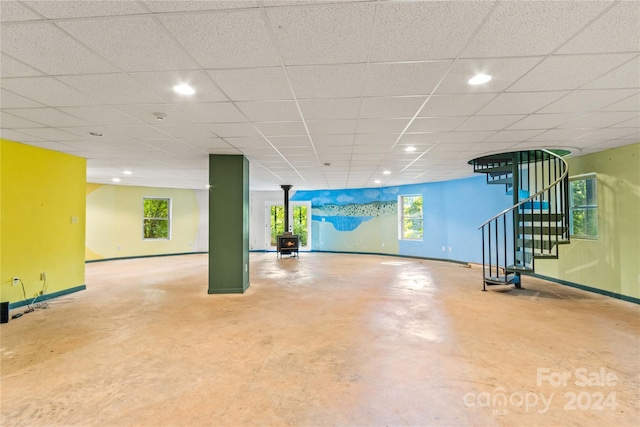 basement featuring stairs, a wood stove, baseboards, recessed lighting, and a paneled ceiling