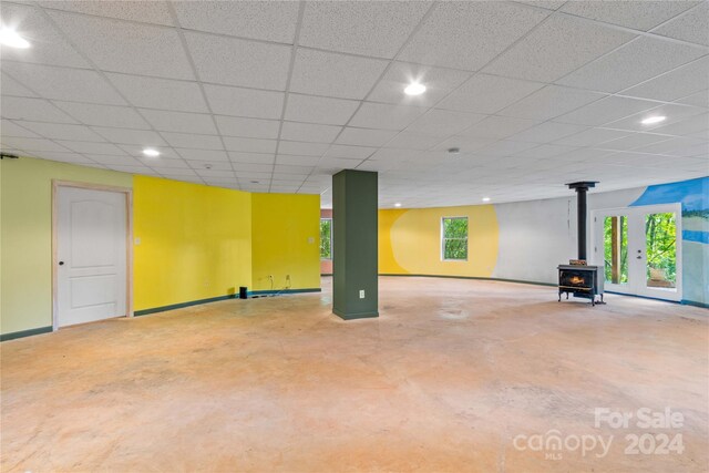 below grade area featuring a drop ceiling, a wealth of natural light, baseboards, and a wood stove