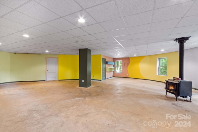 basement with a paneled ceiling, a wealth of natural light, baseboards, and a wood stove